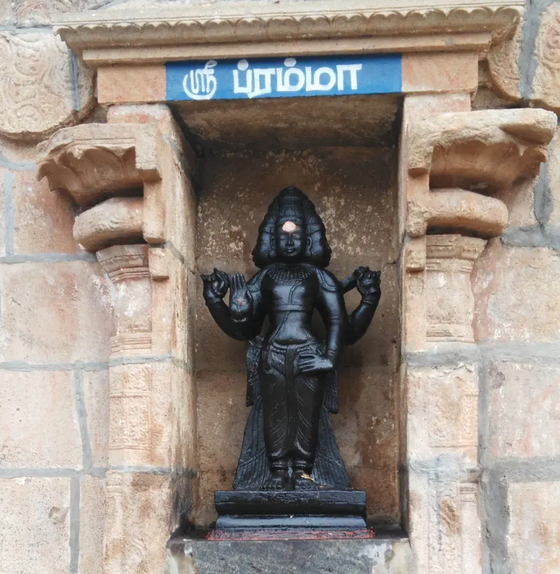 Dark four-armed figure with several faces on a low base, under a blue Tamil name board