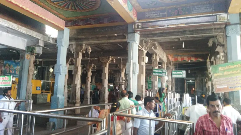 Pillared hall with painted ceiling, steel queue railings and devotees walking through