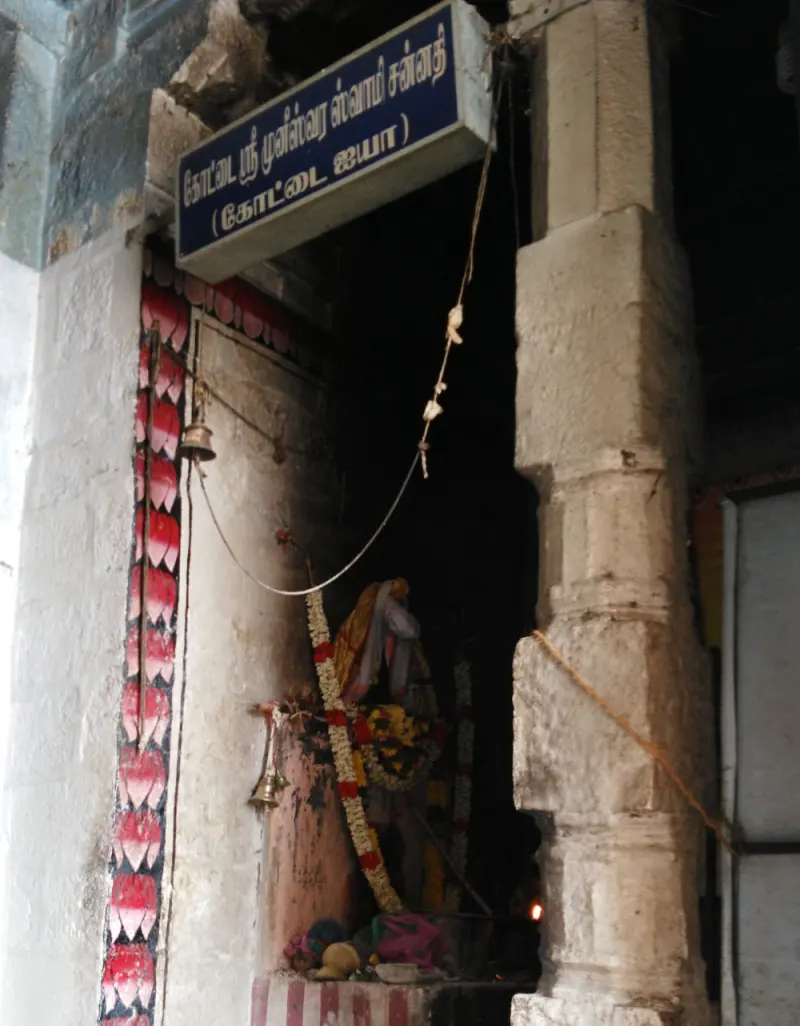 Small dark shrine with a signboard, bells and garlands