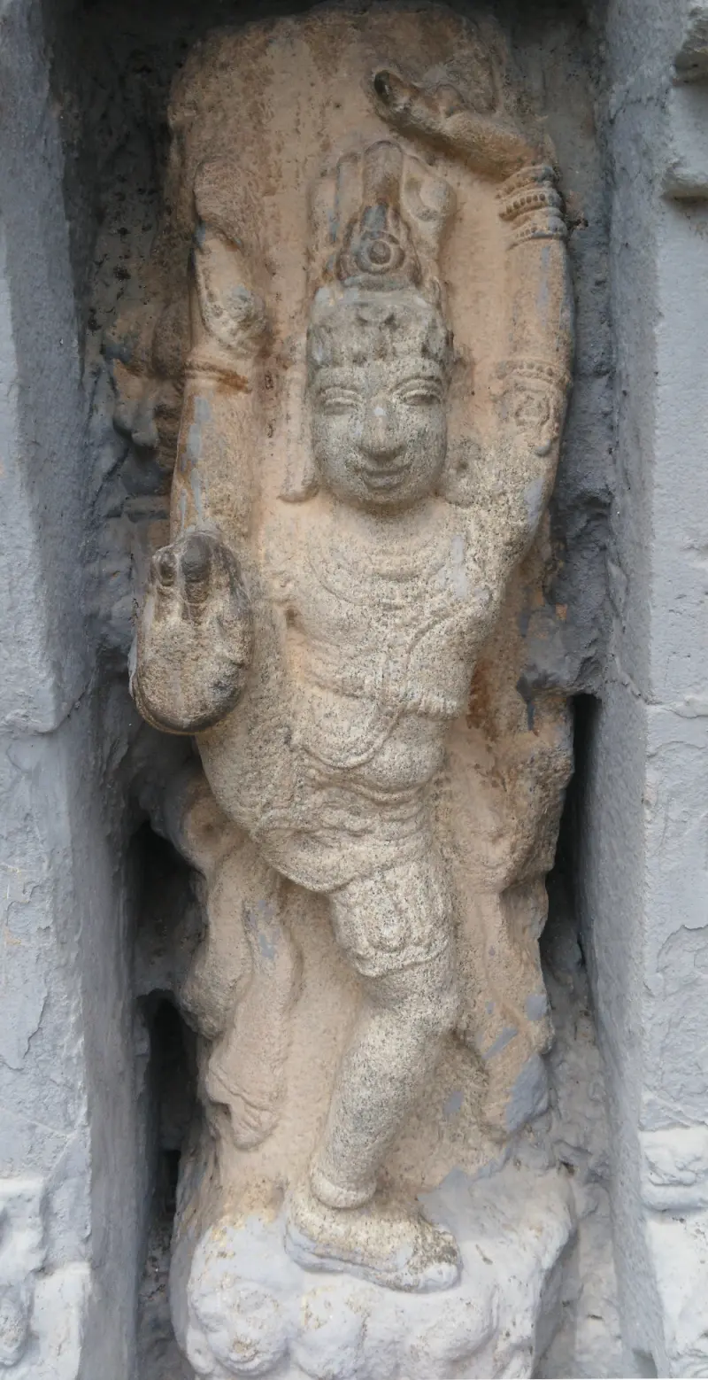 A weathered stone Shiva dancing with one leg raised in a niche