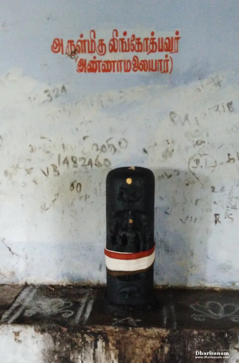 A carved figure on a tall stone, with the name painted in red Tamil letters above