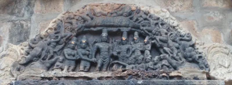 A weathered stone relief under an arch with a group of standing figures at the centre and smaller figures around them.