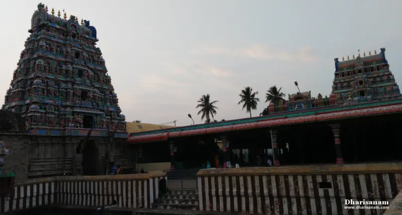 Two tiered gopurams behind a striped tank wall and a long pillared hall, with palm trees between