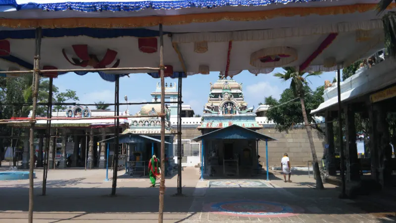A small shrine and a tower seen from under a canopy, with kolam patterns on the floor.