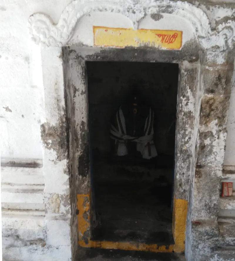A dark shrine doorway framed in whitewashed stone with a yellow board above, and a draped image inside.