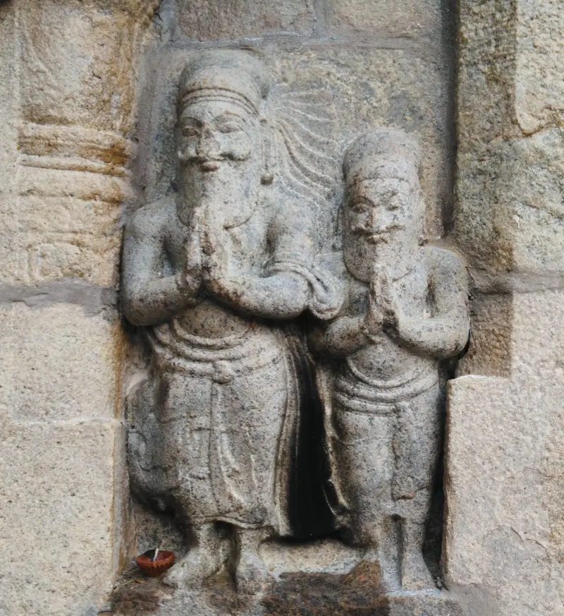Two bearded stone figures with palms joined, carved in a niche, with a small lamp at their feet.