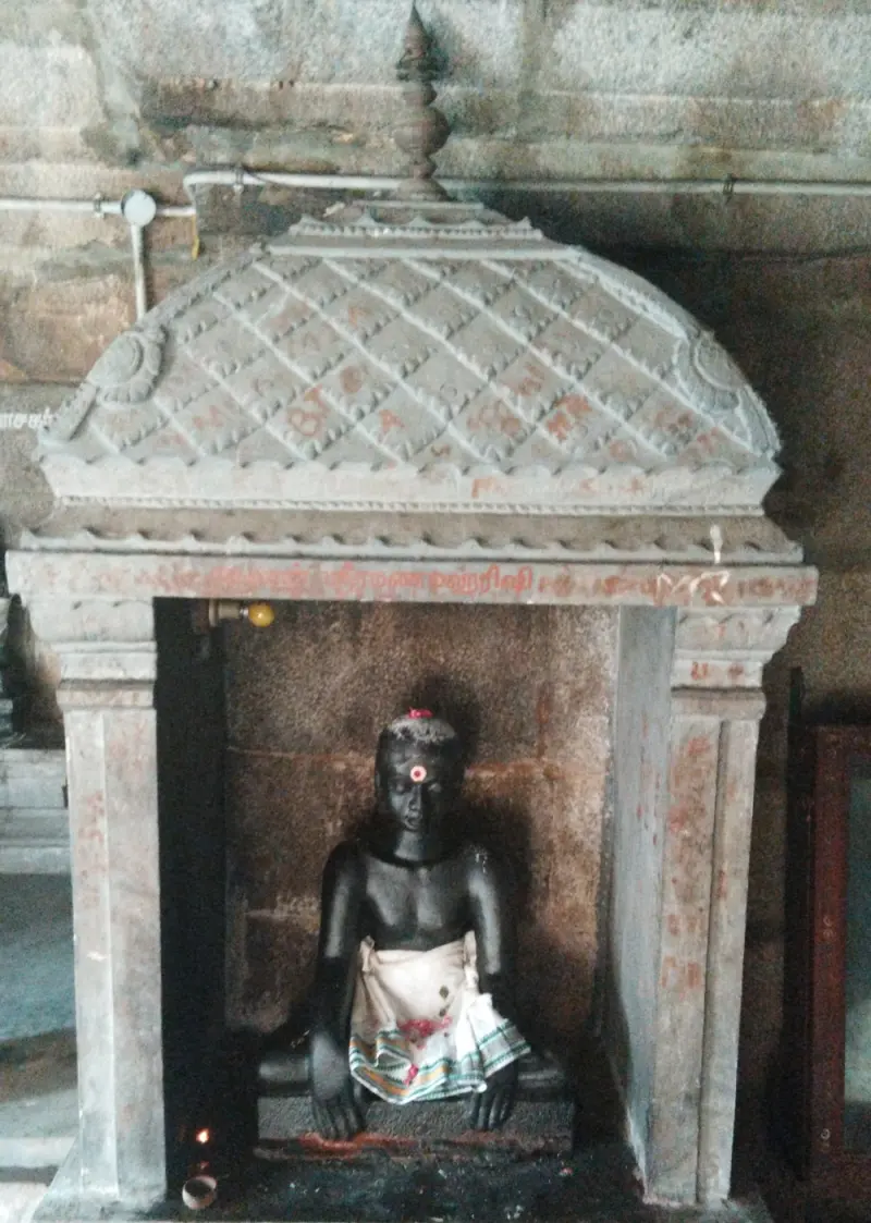 A seated black stone figure of a young boy in a cloth, in a small stone shrine with a lamp
