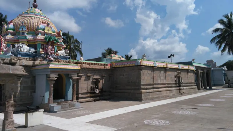 A wide paved courtyard beside a long stone corridor, with a colourful shrine dome at the far end