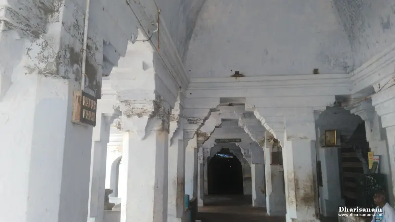 White-washed pillared hall with arches leading towards a dark doorway