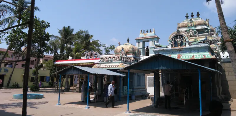 Shrines with painted towers in the courtyard, a visitor walking past a blue-pillared shelter.