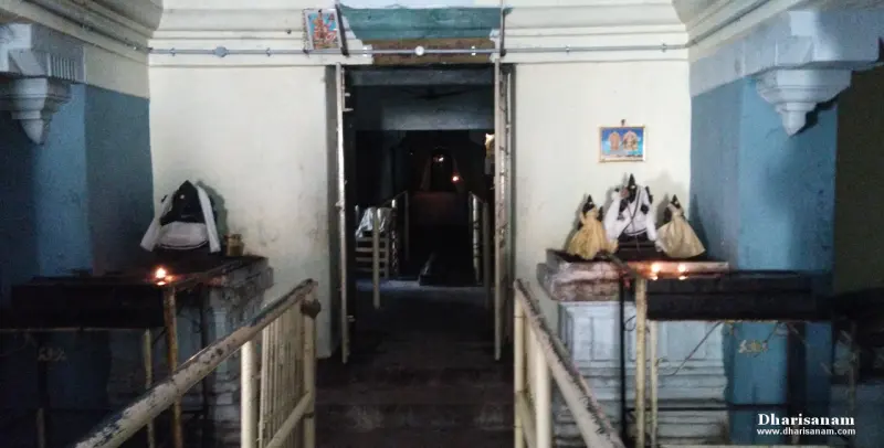 A narrow passage with railings leading to a dark doorway, with lamps and idols on platforms on both sides