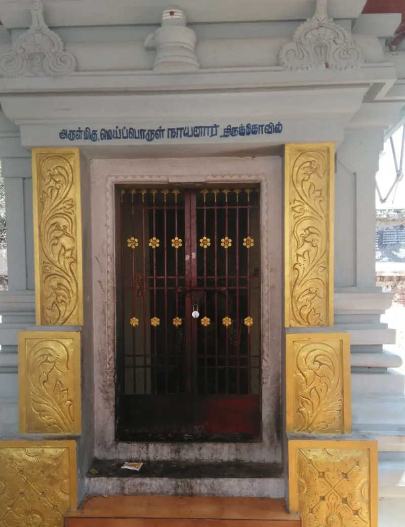A small grey shrine with gold-painted panels, a locked grille door and a Tamil name board above