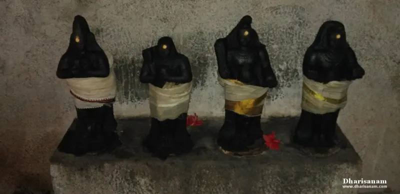 Four small dark idols standing in a row on a stone platform, each wrapped in cloth.