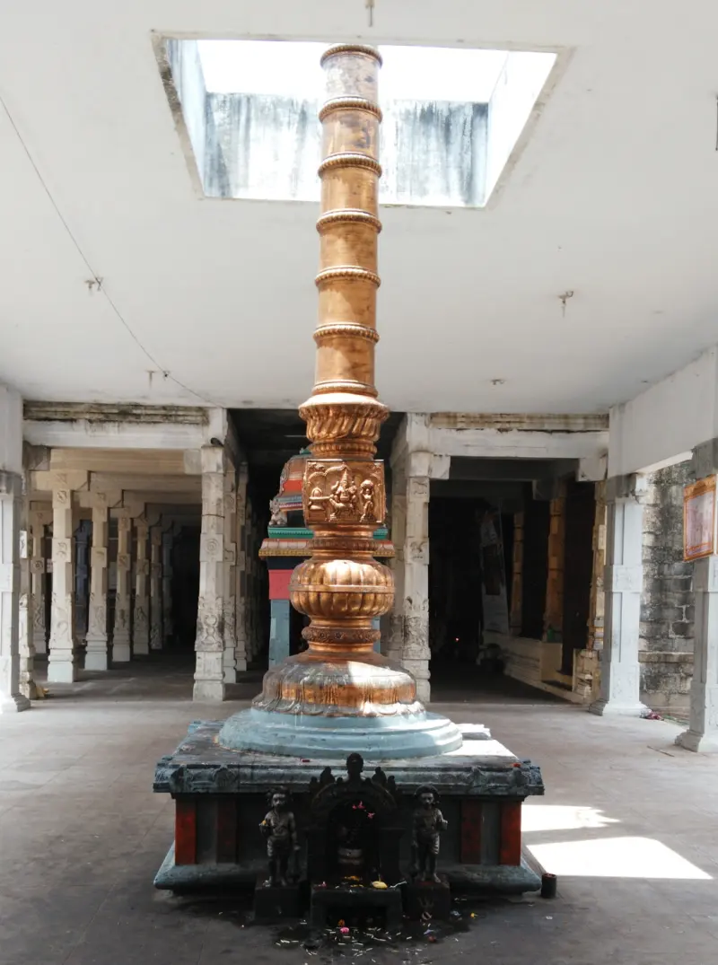 A gold-coloured pillar rising to a skylight in a pillared hall, with small figures at its base