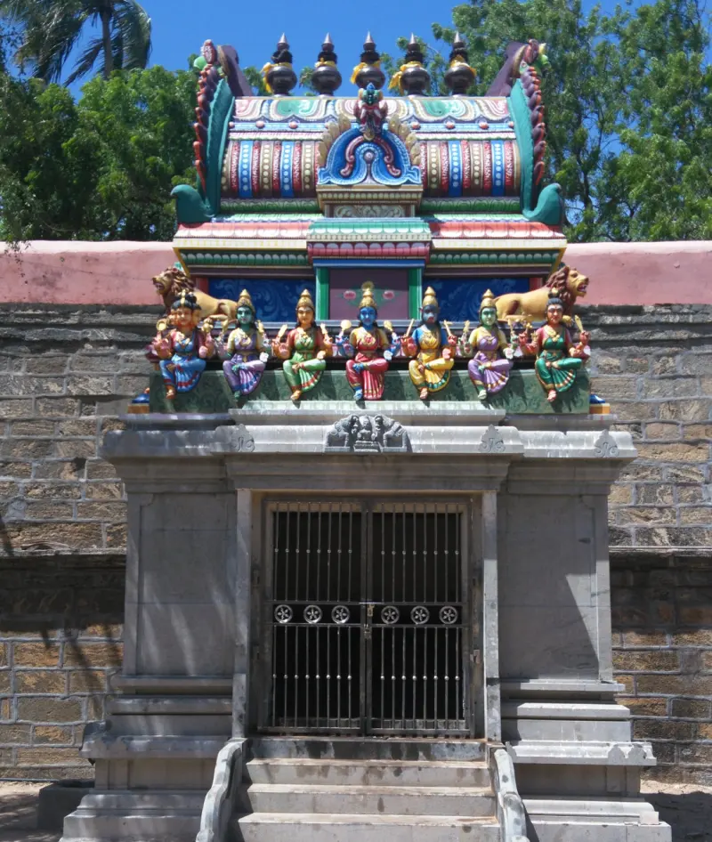 A shrine with a barred door and steps, and a row of painted goddess figures seated along its roof.
