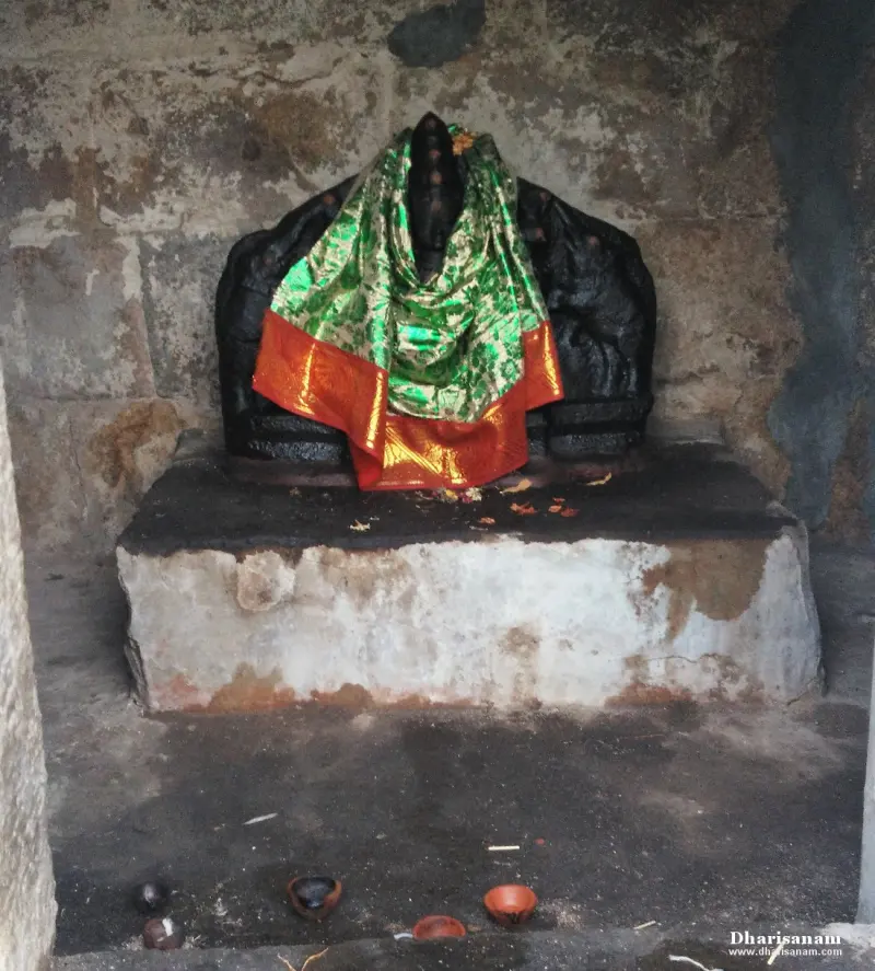 A dark stone idol on a platform, draped in a green and orange silk cloth, with small lamps at its base.
