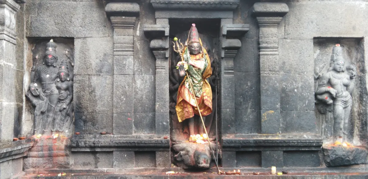 A stone niche holds a standing goddess in colourful cloth with a trident, between two relief figures.