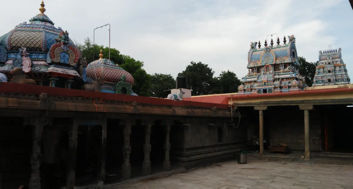 Stone courtyard with two domed shrine roofs on the left and painted towers beyond a pillared corridor