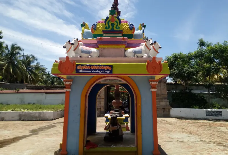 Colourful small shrine with white bulls on the roof and an image inside, under a Tamil name board