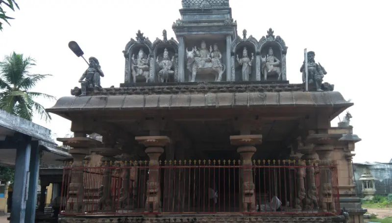 A stone shrine behind a red railing, with sculpted deities in niches along the top and a guard figure at each end.