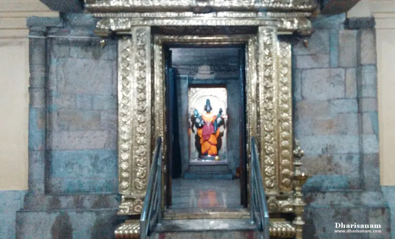 A gold-toned carved doorframe with steps, and a deity in orange cloth standing inside the shrine