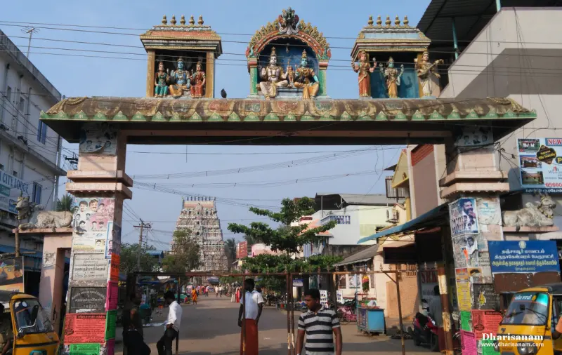 A painted arch with sculpted deities over a busy street, the temple tower visible far beyond