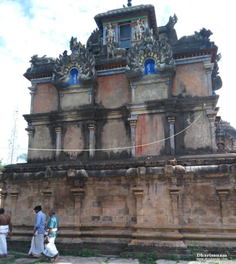 A tall stone building with painted upper walls and a carved roof, and three men walking by