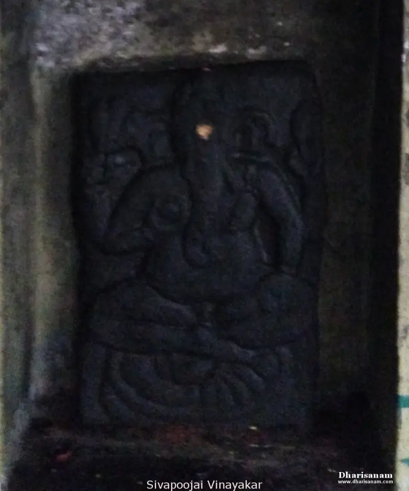 A dark stone relief of a seated Vinayakar in a niche