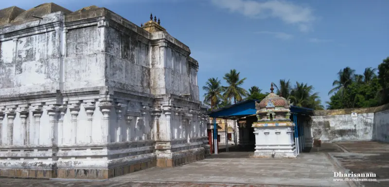 A whitewashed shrine building with carved pillars beside a small blue-roofed shrine with a coloured dome