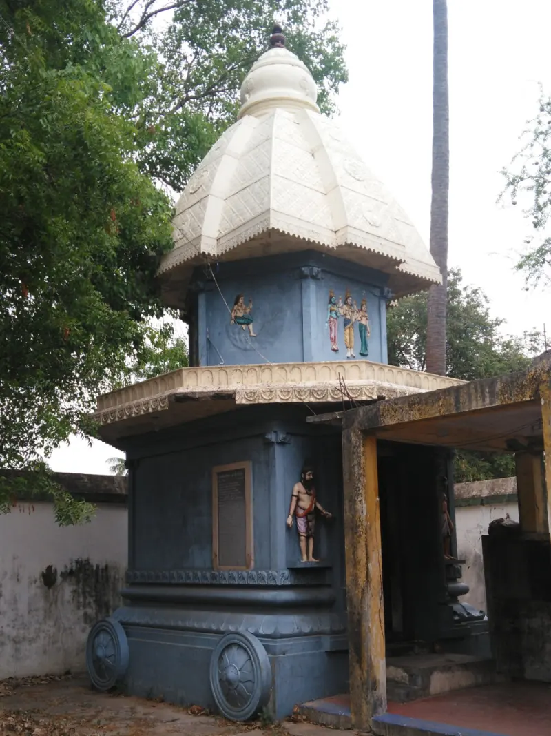 A blue shrine on stone wheels with a white dome and painted figures