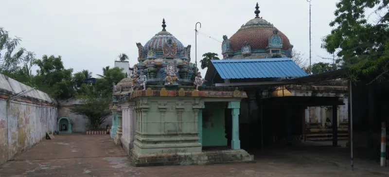 A courtyard with two domed shrine roofs, trees around, and a blue metal roof over part of the corridor.