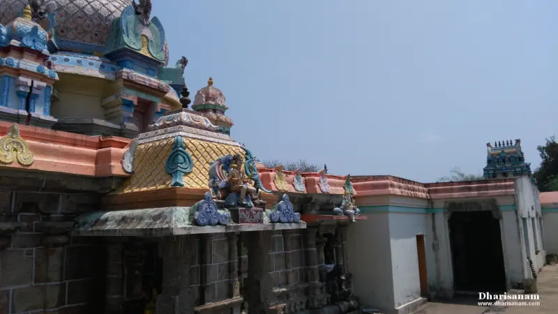 A stone shrine wall with a colourful roof and stucco figures, a white wall to the right, a tower far off