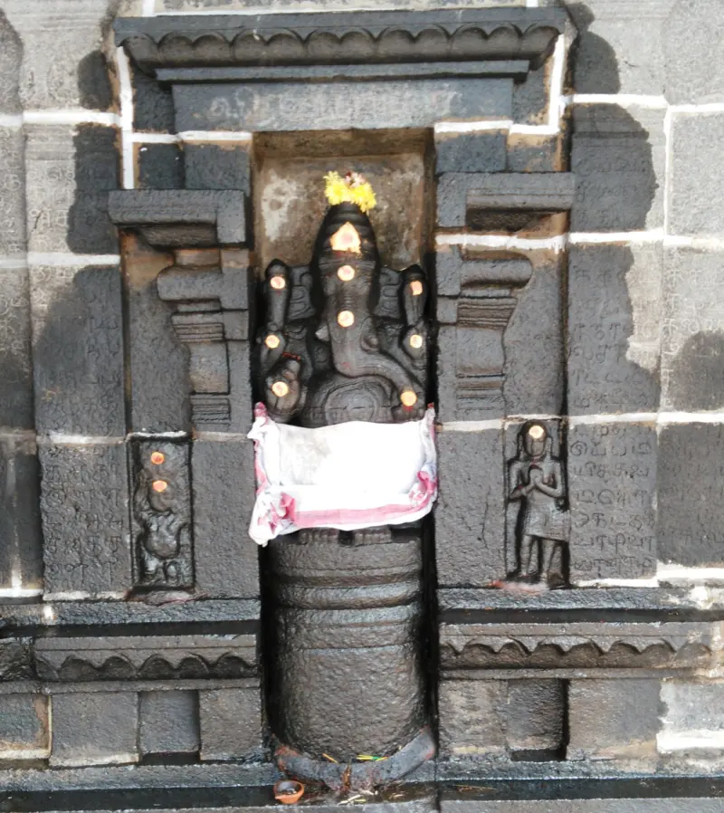 Black stone Vinayakar in a wall niche, with a white cloth and lit oil lamps