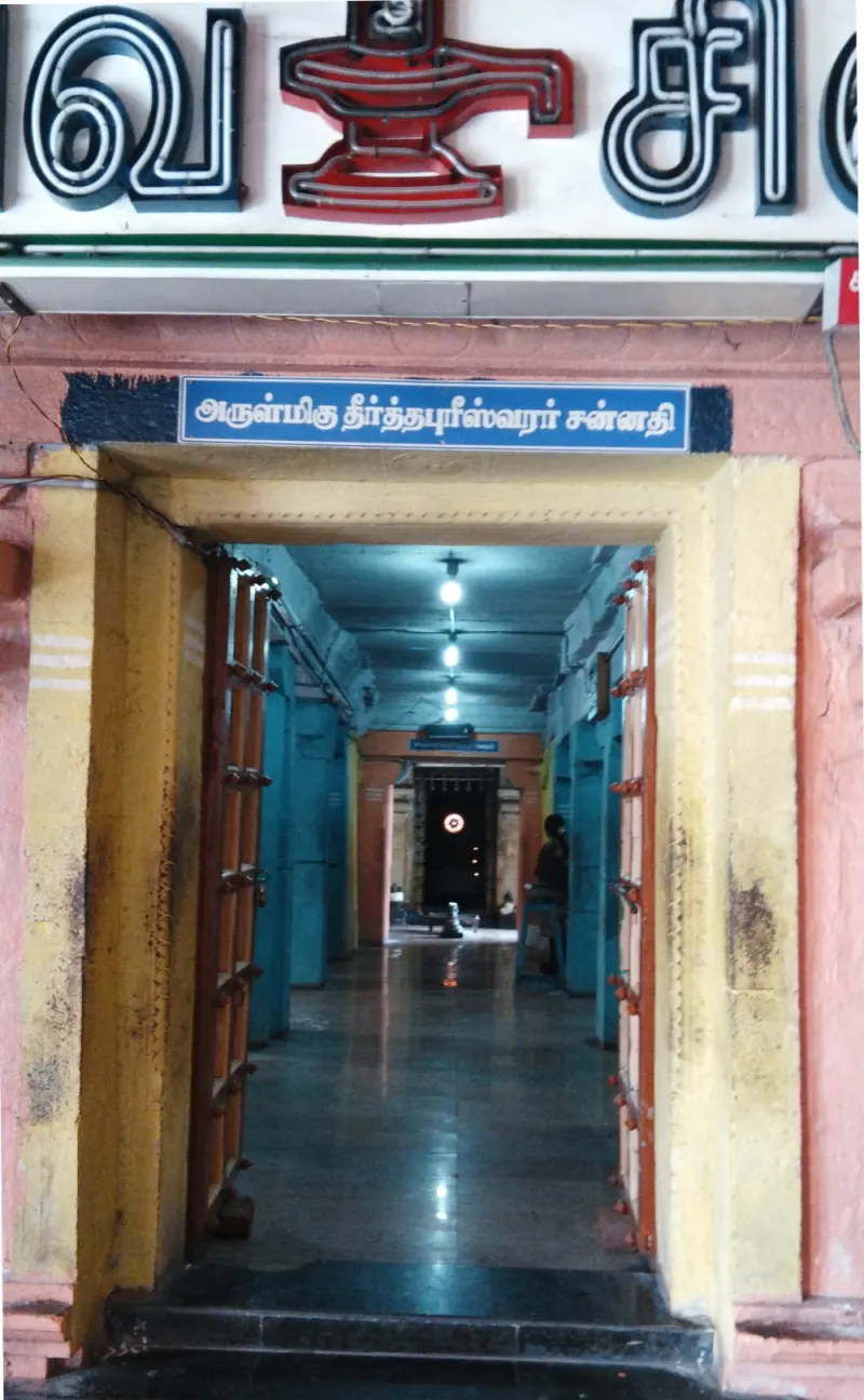 Open doorway with a blue Tamil name board, leading to a lit corridor