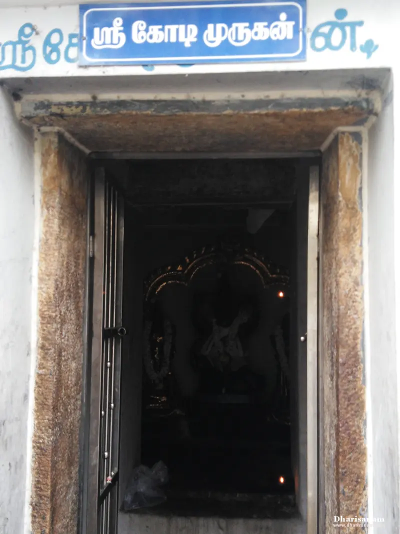 A narrow shrine doorway under a blue board reading Sri Kodi Murugan, with a dim idol within