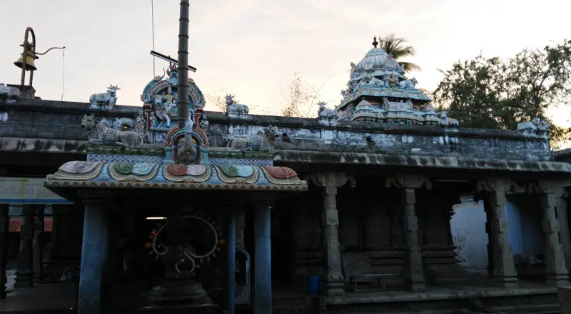 Tall flagstaff and a painted canopy before a pillared hall with a tower