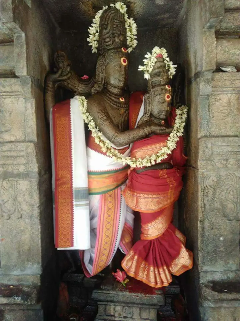 Garlanded stone idol of a standing god in white cloth, with a smaller figure in red silk at his side