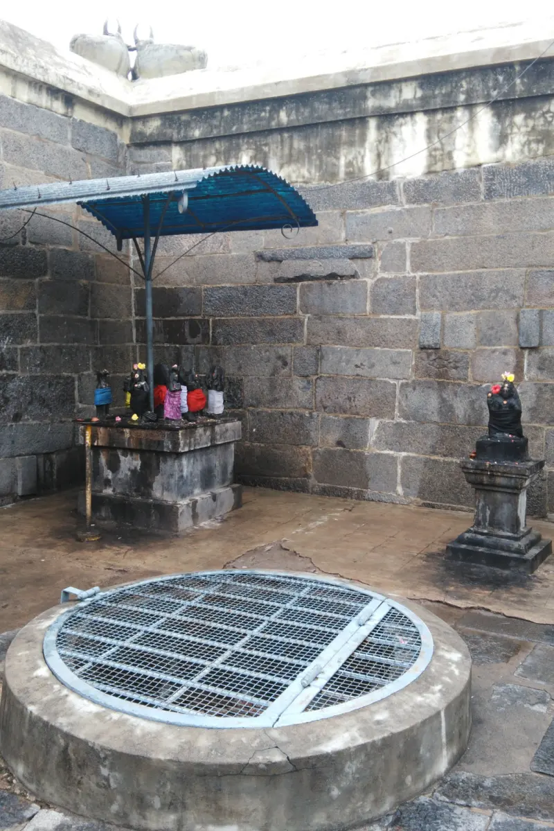 A round well with a metal grille, small dark images on a stone platform under a blue roof, and one on a pedestal.