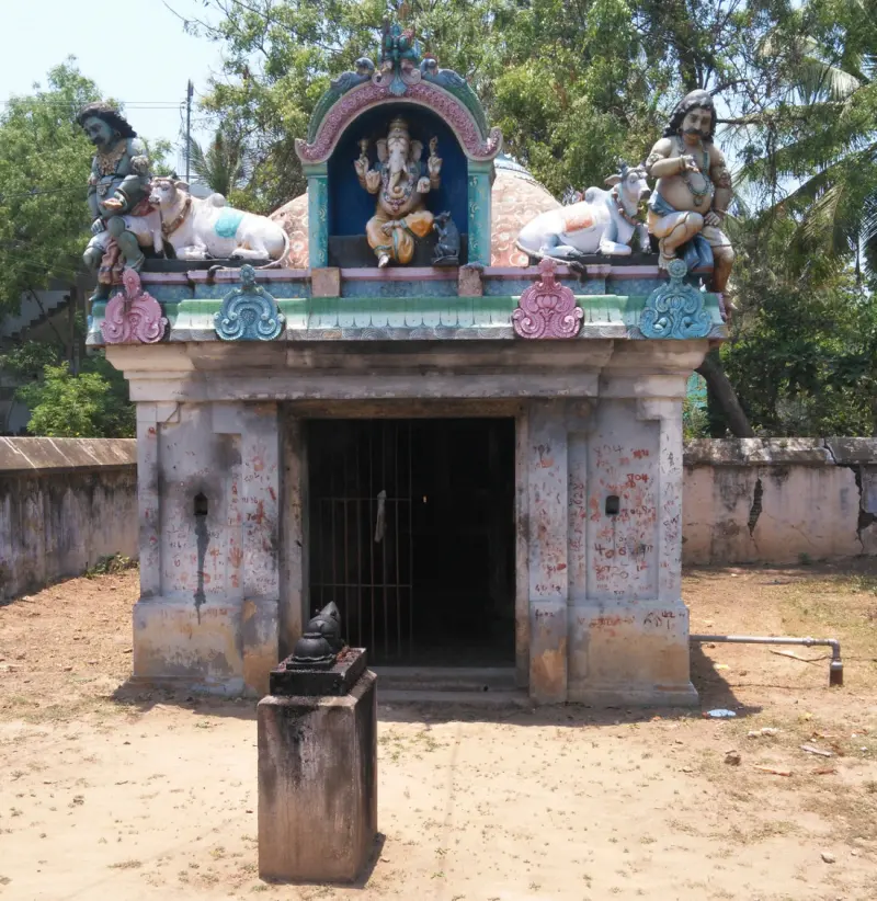 A small shrine with Vinayakar in a niche, two bulls and two figures on the roof, a stone pillar in front.