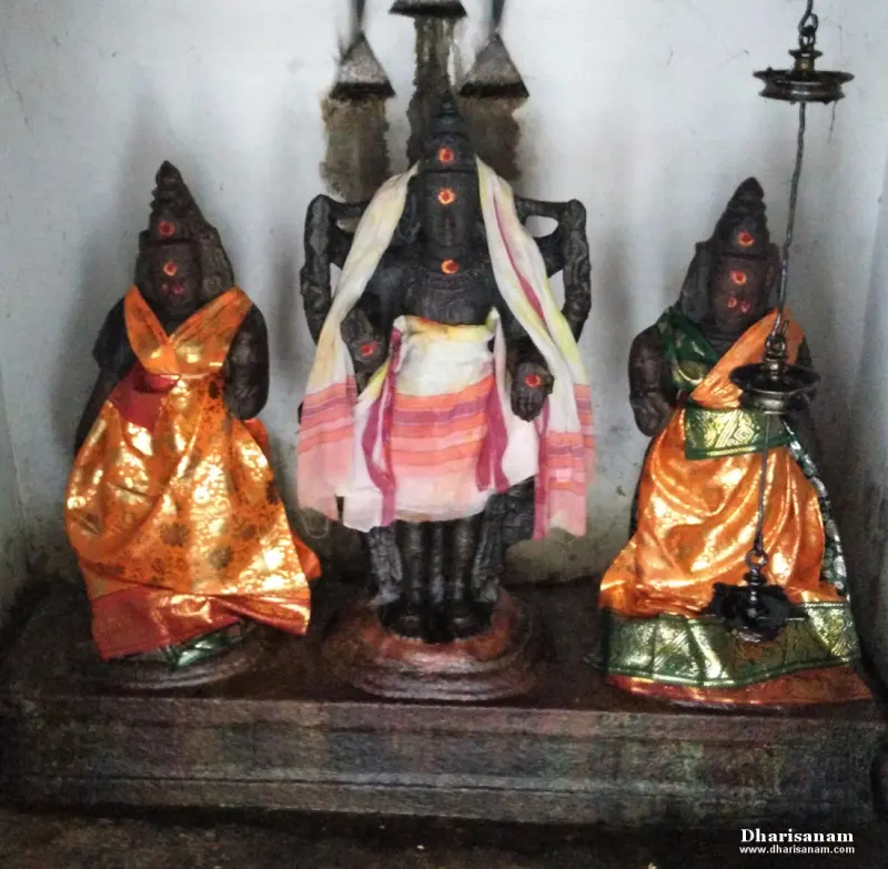 A tall dark idol with a striped cloth stands between two seated idols dressed in orange and green silk