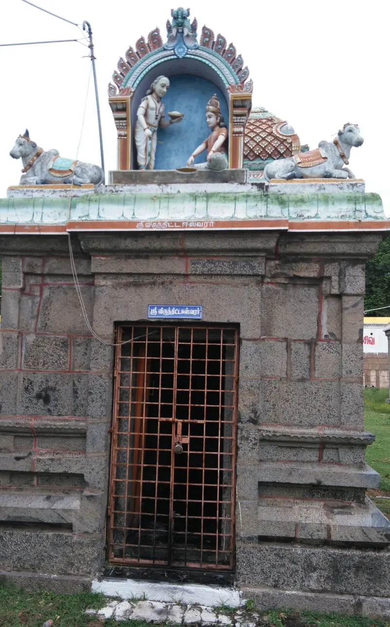 A small stone shrine with an iron gate, and above it figures of an old man offering a bowl to a seated man.